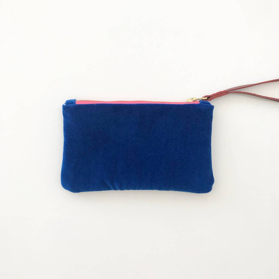 Ellie wristlet in deep blue velvet, showing bright pink zipper with brass pull and brown leather strap, flat lay front view.