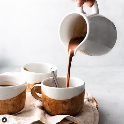 
                    
                      Organic Dark Drinking Chocolate poured into a two-tone speckled ceramic mug with a whisk, two other mugs on a linen napkin.
                    
                  