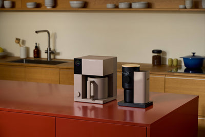 
                    
                      Fellow Opus 2 Conical Burr Grinder, beige and black with wood top, on a reddish kitchen counter.
                    
                  