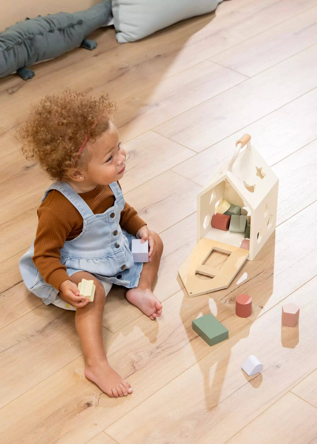 Wooden Shapes Sorting House, natural wood, pastel blocks, child playing with star shape, side view with hinged base open.