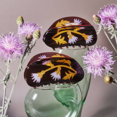 
                    
                      Milk Thistle hair claws, deep brown cellulose acetate with gold and lavender thistle pattern, pair displayed amongst purple…
                    
                  
