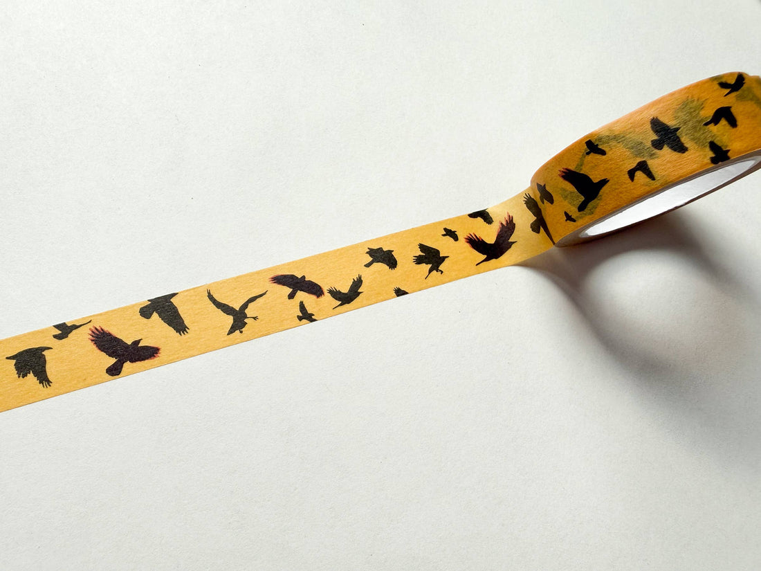 Flying Crows washi tape in yellow, black bird pattern on rice paper, partially unrolled, angled close-up view.