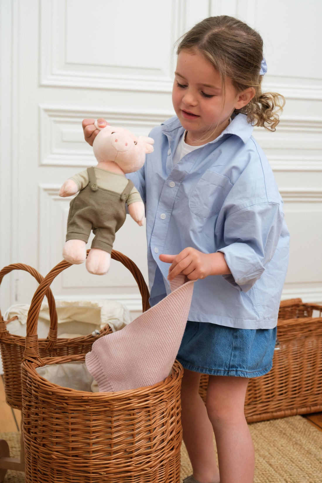 Egmont Wicker Shopping Caddy, natural woven willow, child placing pink blanket and pig toy inside for scale.