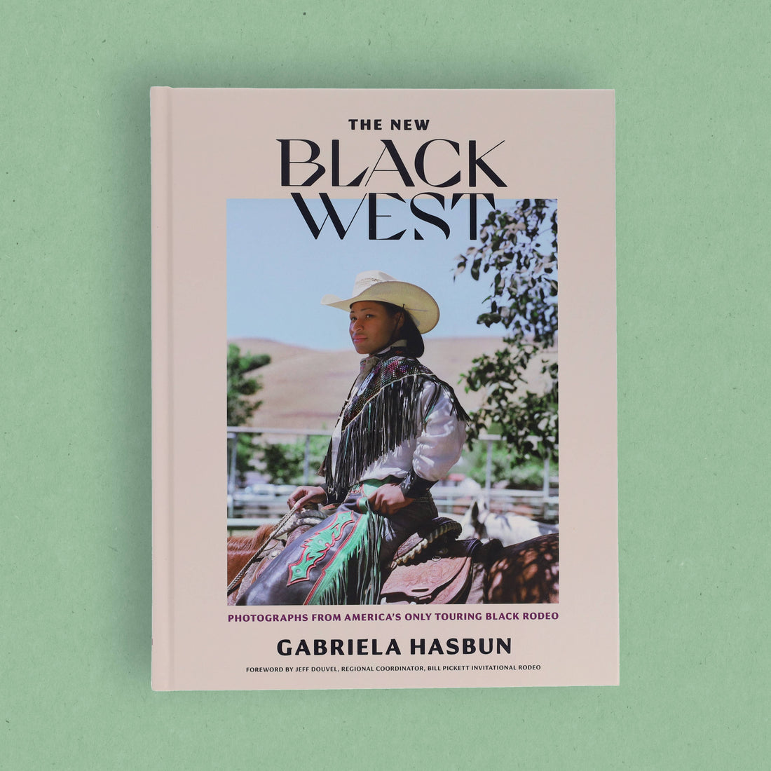 The New Black West book, full front cover featuring a cowboy rider, light pink cover, flat lay on green background.