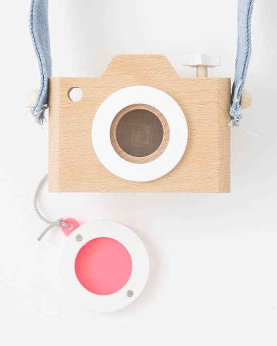 Kaleidoscope Play Camera toy, natural beechwood body with blue strap, white kaleidoscope lens, and separate bright pink…