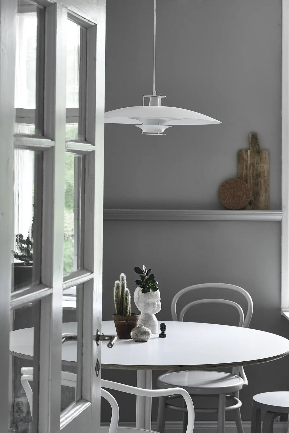 Green Home Book: bright living space with white round table, chairs, potted cactus, plants. Scene viewed through open door.