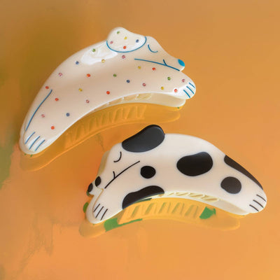 
                    
                      Puppy Claw Spotted Dog hair clip, white cellulose acetate with black spots, paired with polka dot version, flat lay.
                    
                  