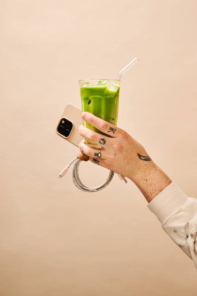 
                    
                      Iced Ceremonial Matcha, bright green, in a tall glass with straw, held in hand with a phone.
                    
                  