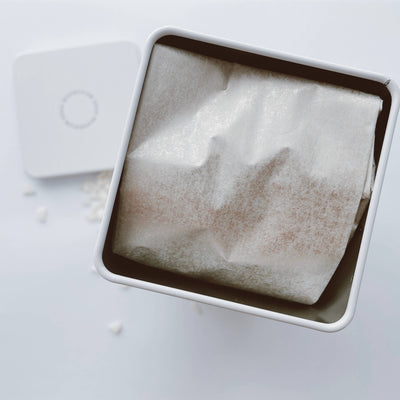 
                    
                      Magnesium Bath Soak, open white tin with translucent tissue paper and scattered white magnesium flakes, top-down view.
                    
                  