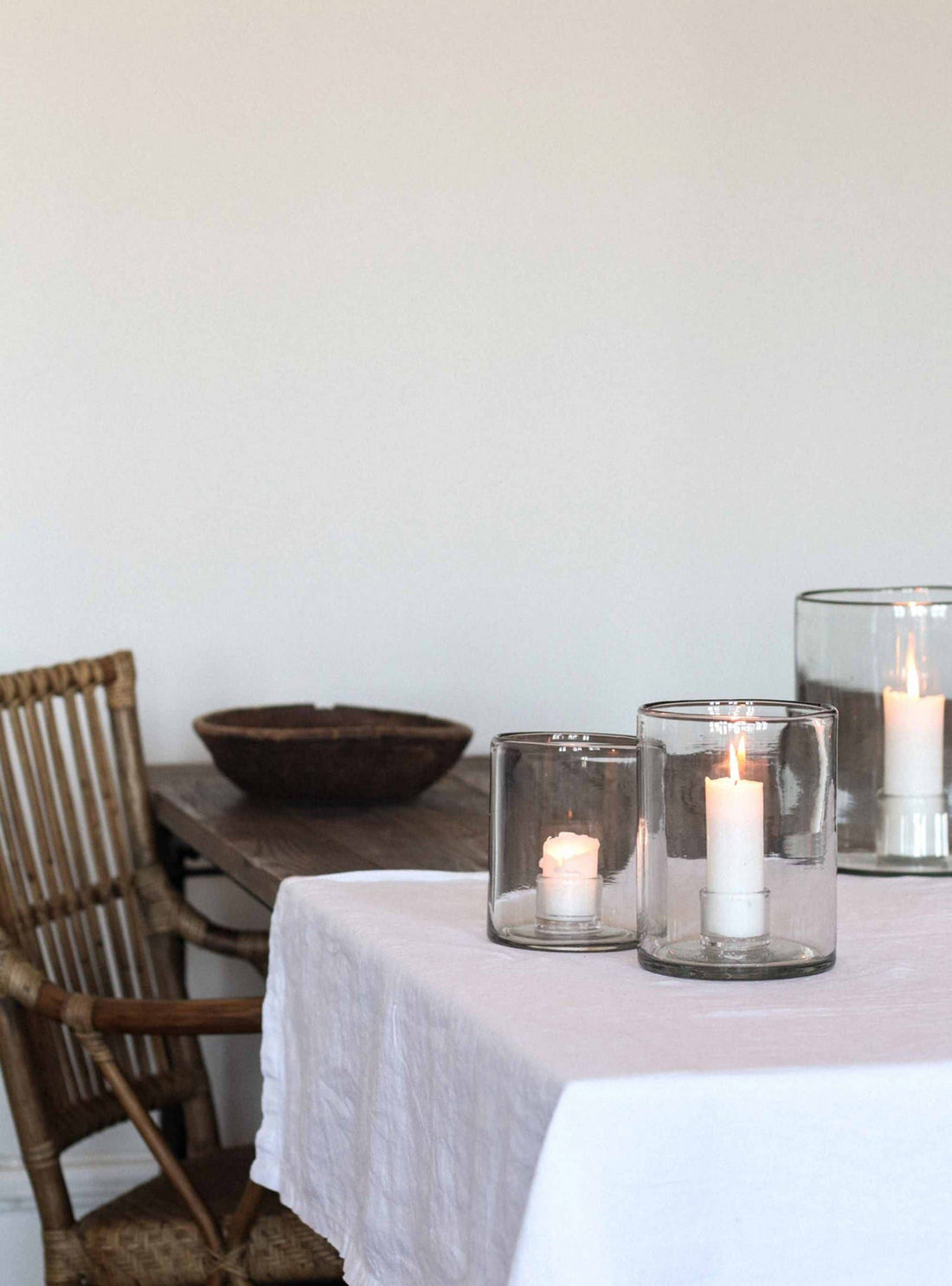 Multiple White Pillar Candles, lit in clear glass hurricane lamps, arranged on a white tablecloth.