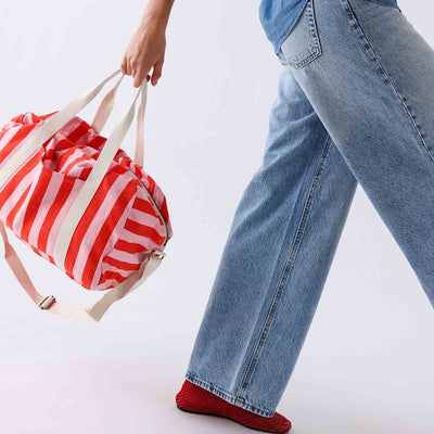 
                    
                      Raphael diaper bag, tomato & candy pink stripes, cotton fabric, carried by hand by person walking, side view.
                    
                  