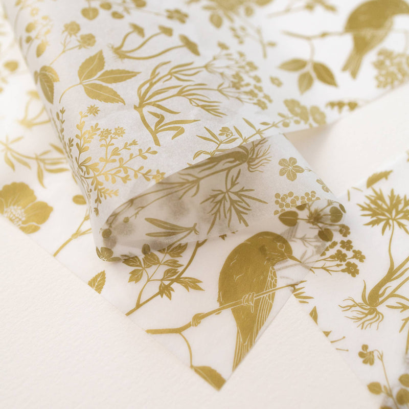 Botanica Paper Co. Gold Meadow tissue paper, gold botanical and bird pattern on translucent white, partially unrolled.