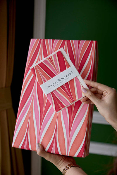 
                    
                      Candy Stripes Sugar Spice wrapping paper, red, pink, white recycled cotton, hand holding branded sample against gift.
                    
                  