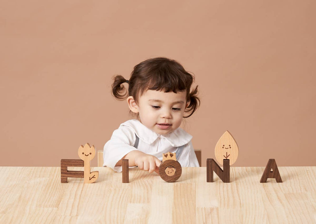 Wooden Alphabet Play Blocks, Beech and walnut wood with etched character faces, child playing on table, demonstrating scale.