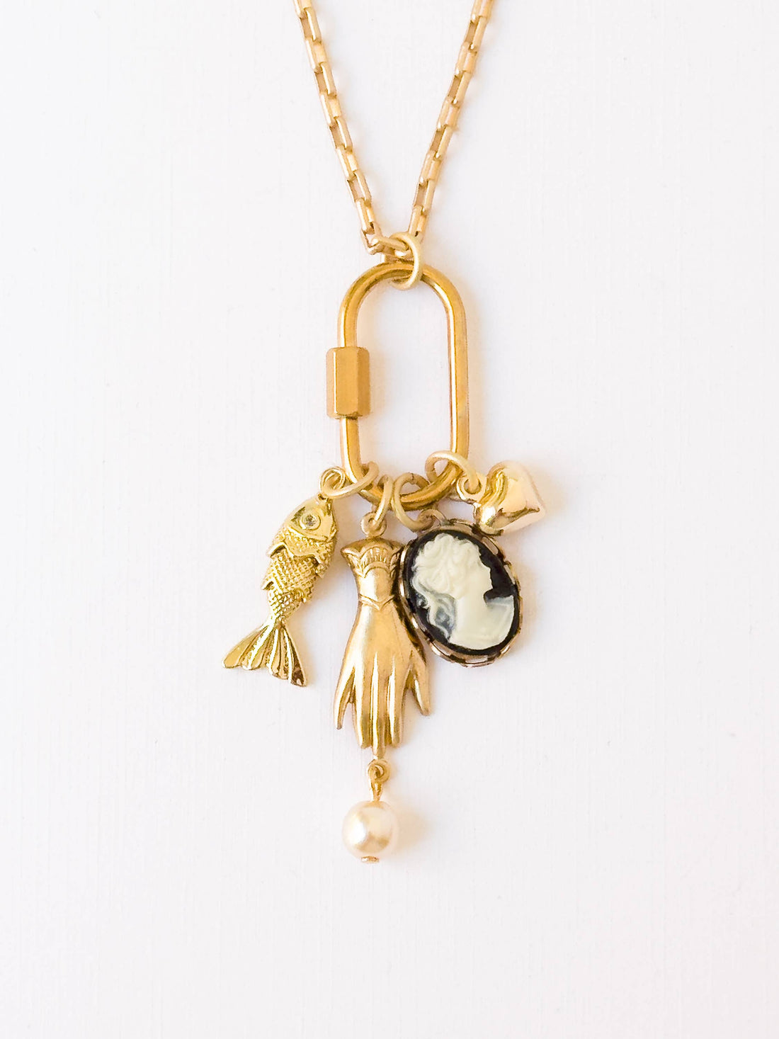 Cameo & Fish Charm Necklace, close-up of gold-plated carabiner with hand, black cameo, fish with crystal, and pearl charms.