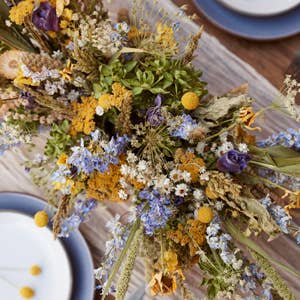 Designing with Dried Flowers book, close-up of a centerpiece with yellow, blue, and purple dried flowers on a table.