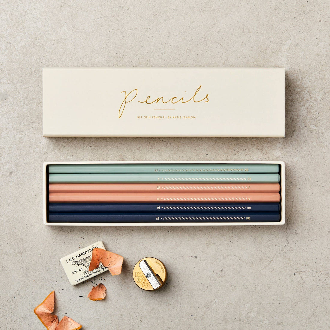 Katie Leamon Assorted Box of Pencils (set of 6) in muted blue, green, peach. Open box flat lay with gold sharpener & wood…