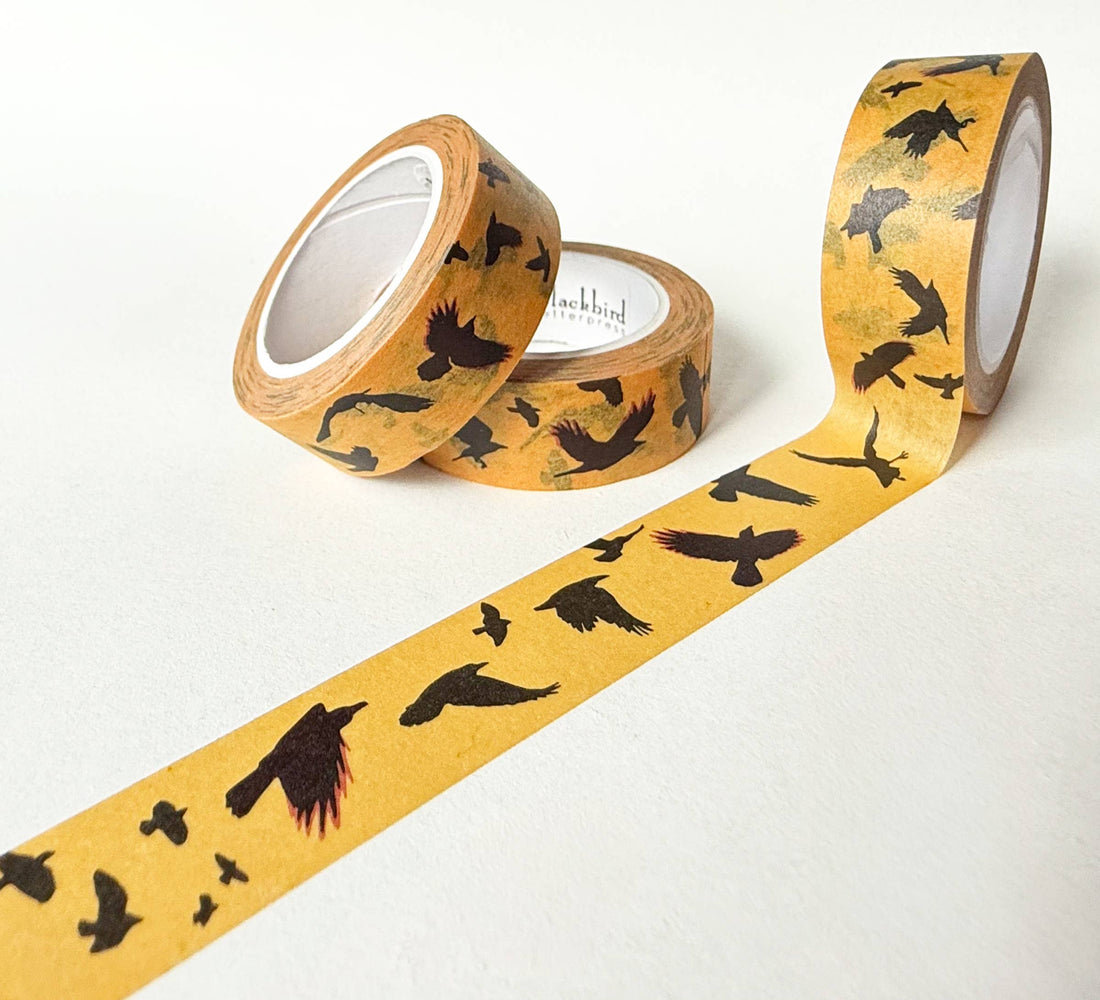 Flying Crows washi tape, mustard yellow rice paper with black crow silhouettes. Two rolls, one unrolled to display the full…
