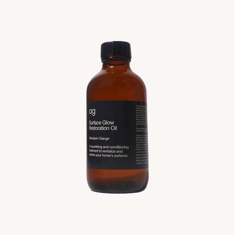 Surface Glow Restoration Oil, brown glass bottle with black cap, black label with Mandarin Orange scent, angled front view.