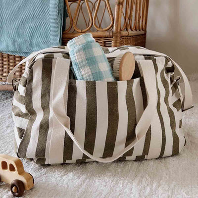 
                    
                      Raphael Weekend diaper bag, olive and greige striped 100% cotton, open top with blue blanket and wooden brush visible.
                    
                  