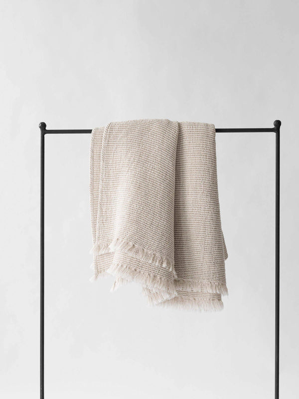 Tell Me More Calma Waffle-Weave Blanket, natural cotton-linen, fringed, draped over black rack.