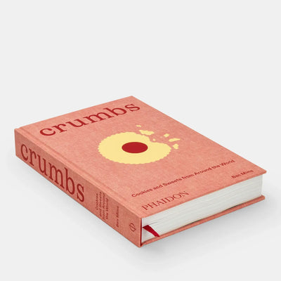 
                    
                      Crumbs: Cookies And Sweets From Around The World hardcover book, coral fabric cover, yellow cookie graphic, angled view with…
                    
                  