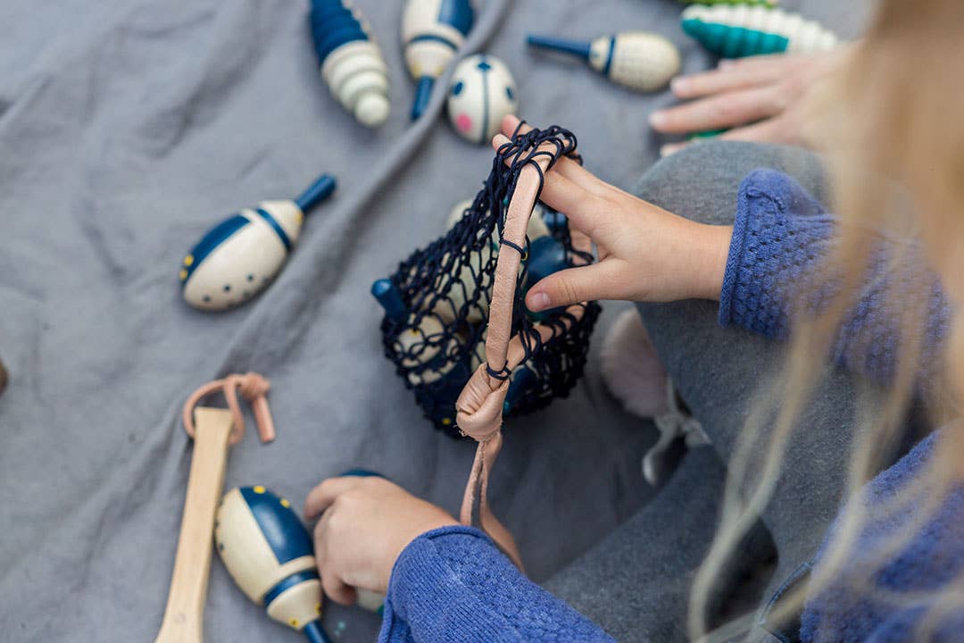 Child's hands hold Hillside Beetles in a dark blue cotton net bag with leather strap. Blue and white painted wooden rolling…