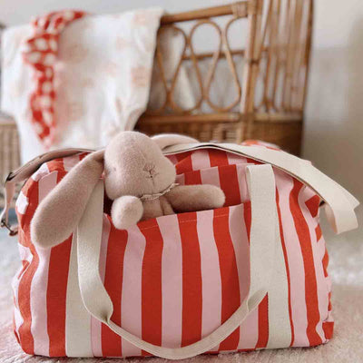 
                    
                      Raphael diaper bag, tomato and candy pink vertical stripes, with a plush bunny toy peeking from a side pocket.
                    
                  
