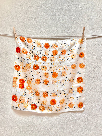 
                    
                      Abby naturally dyed silk bandana scarf, white with orange bundle-dyed flowers and dark specks, full view hanging.
                    
                  