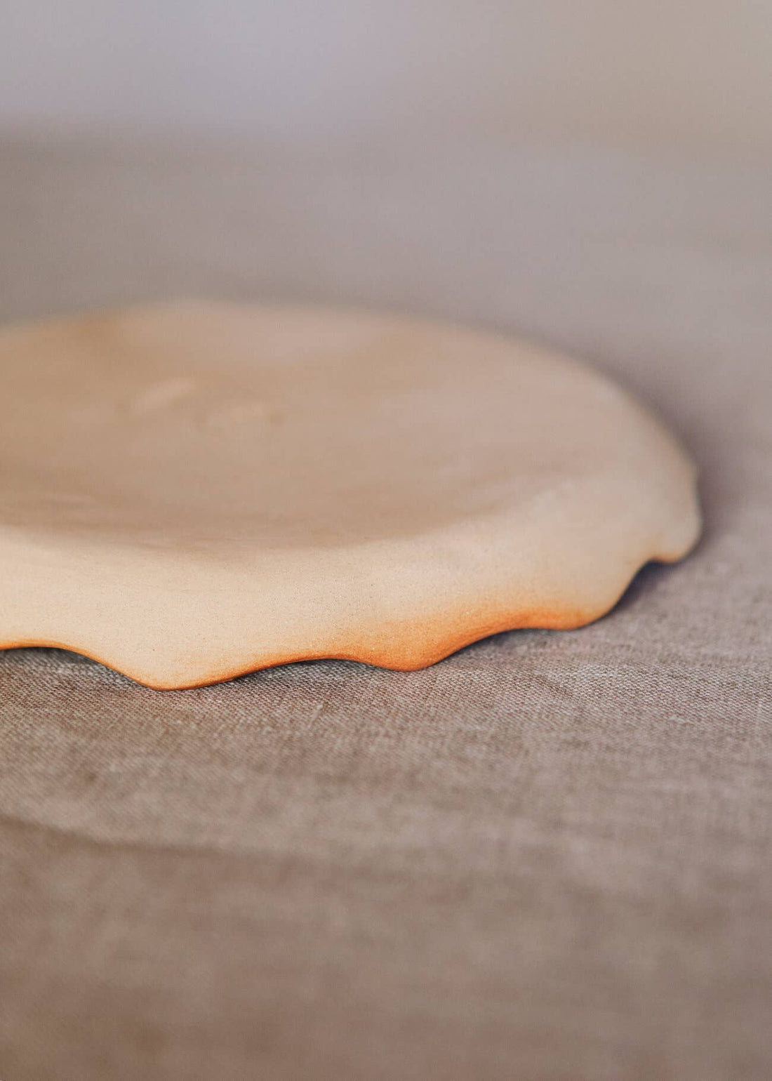 Handcrafted Stoneware Plate, close-up of organic wavy rim, natural light stoneware with reddish-brown fired edge.