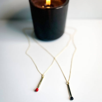 
                    
                      Matchstick necklaces, gold-plated, featuring pendants with red and black matchstick heads, arranged in a flat lay.
                    
                  