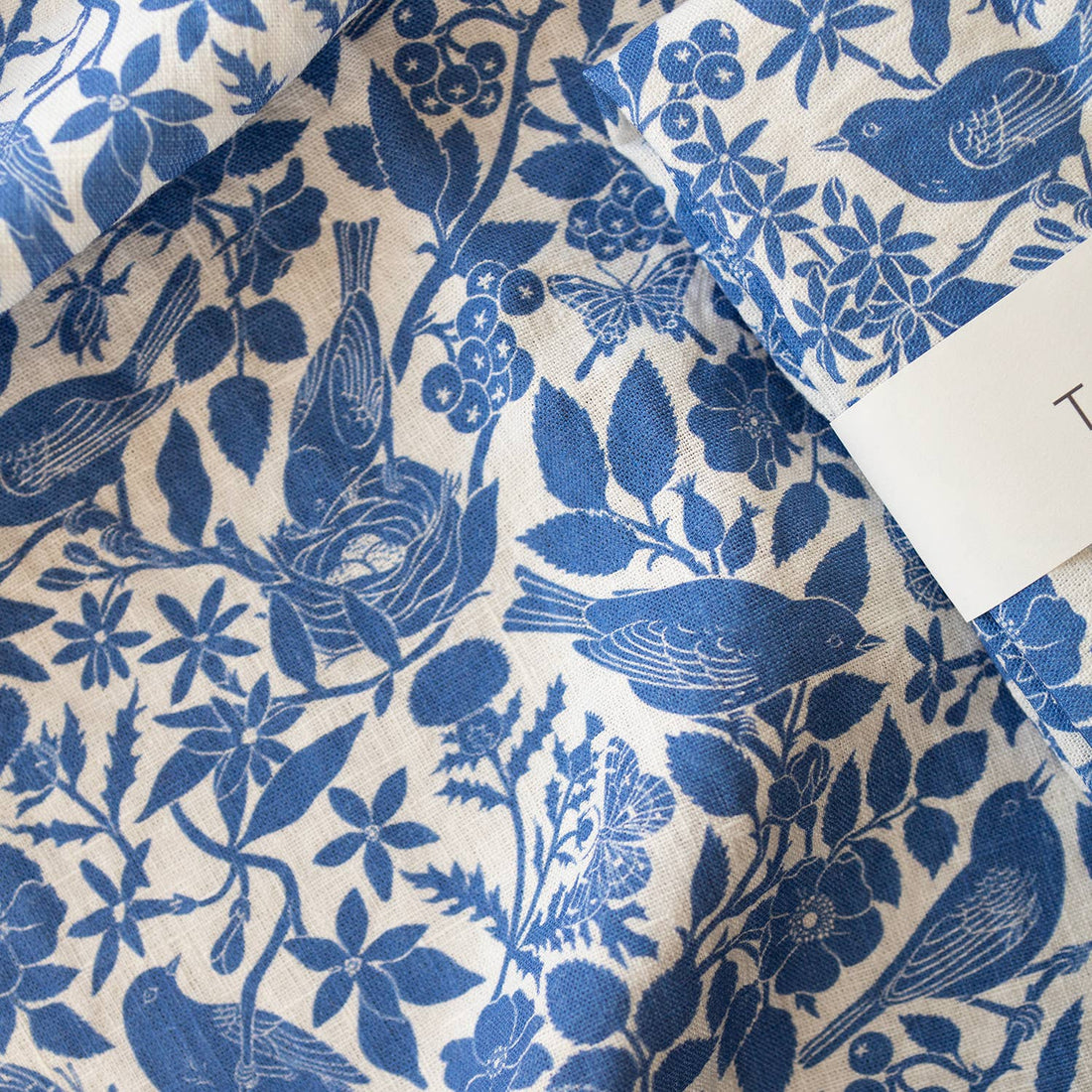 Songbirds Linen Tea Towel, folded close-up of blue bird, berry, and floral pattern on organic white linen.