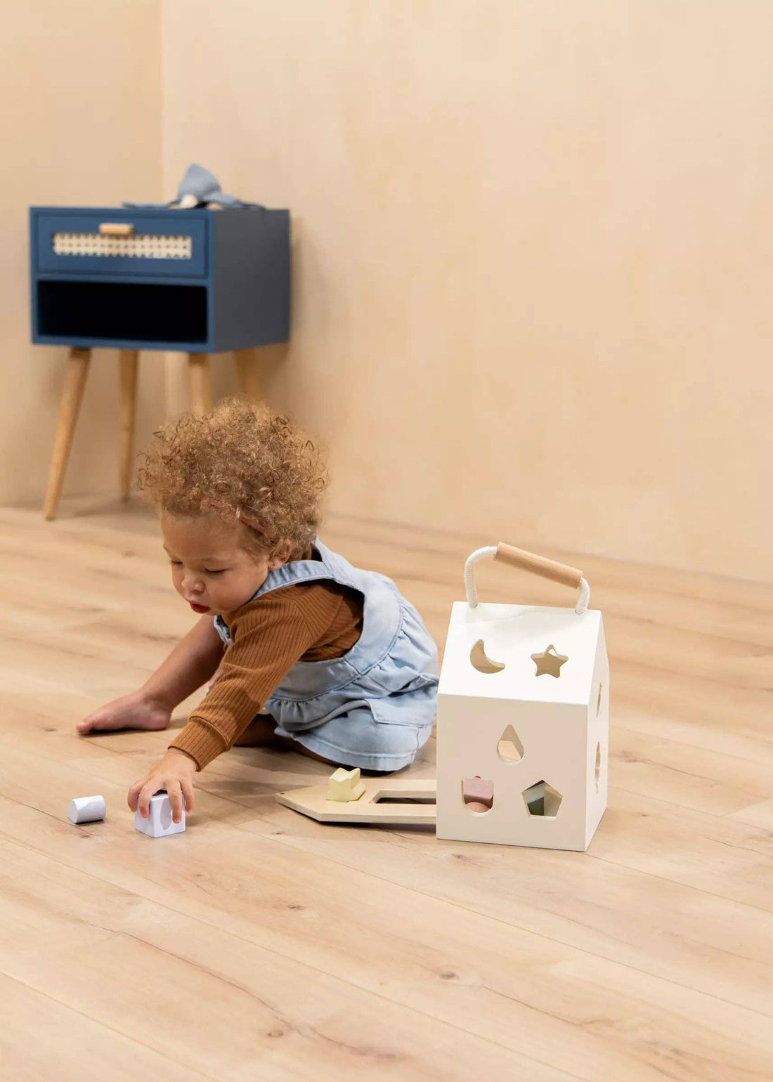 Toddler playing with Wooden Shapes Sorting House, creamy wood house with pastel blocks, on a wooden floor.