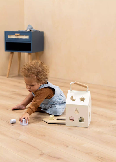 
                    
                      Toddler playing with Wooden Shapes Sorting House, creamy wood house with pastel blocks, on a wooden floor.
                    
                  
