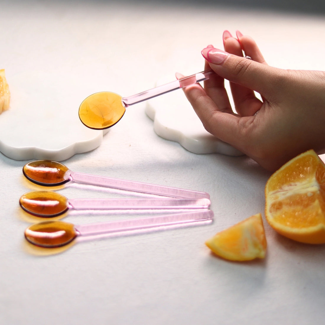Pink and Amber Borosilicate glass stirring spoon held in hand, filling with amber liquid. Three matching spoons, orange…