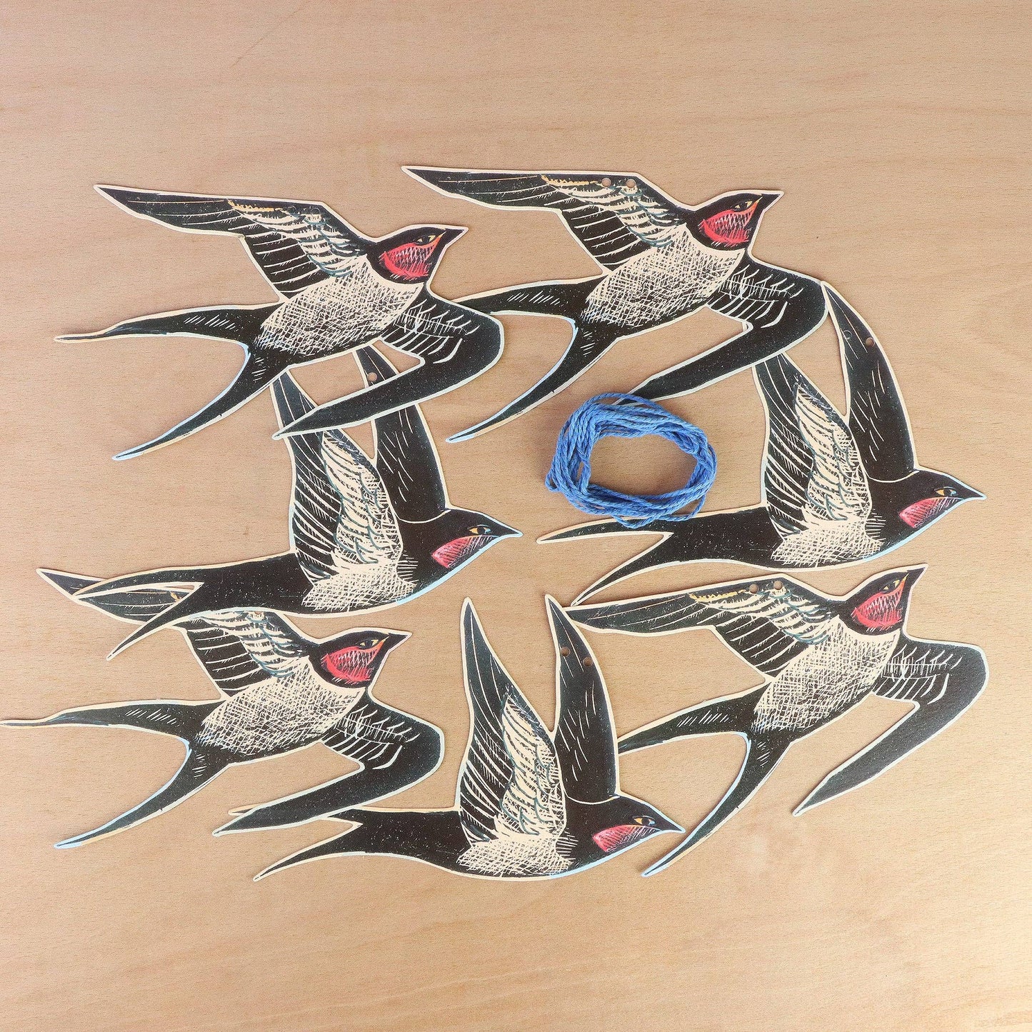 Angela Harding-Cornish Swallows Decorative Paper Garland. Set of black and white bird illustrations with red accents on a beige background, featuring a blue string.