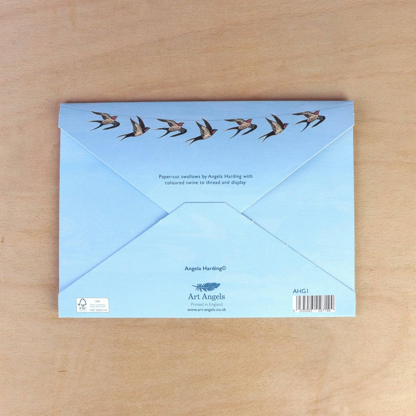 Angela Harding-Cornish Swallows Decorative Paper Garland. Packaging of Blue envelope with paper-cut swallow designs on a wooden surface