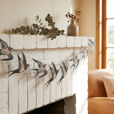 
                    
                      Cornish Swallows Decorative Paper Garland by Angela Harding, black, white, and red paper swallows draped along a white brick…
                    
                  