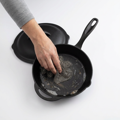 
                    
                      Stainless Steel Cleaning Mesh in use, a hand scrubbing a dirty cast iron skillet with suds.
                    
                  