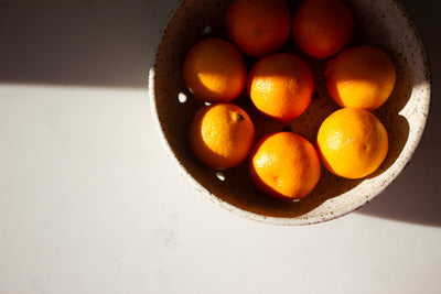 
                    
                      Hand-Thrown Ceramic Colander, speckled natural ceramic, top-down close-up showing textured rim and drain holes, with oranges…
                    
                  