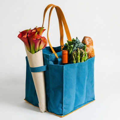 
                    
                      Teal Multi-Pocket Canvas Market Tote with tan vegan leather, filled with fresh flowers, wine, and produce, angled view.
                    
                  