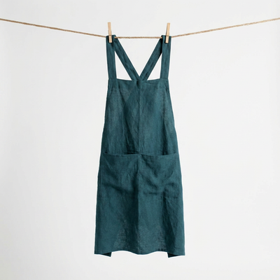 
                    
                      Cross Back Apron, deep teal 100% cotton, hanging full length on a clothesline with visible pockets.
                    
                  