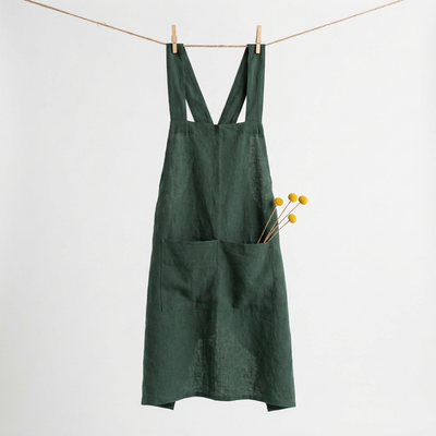 
                    
                      Dark green 100% cotton Cross Back Apron hanging by clothespins on a rope, full front view, yellow dried flowers in pocket.
                    
                  