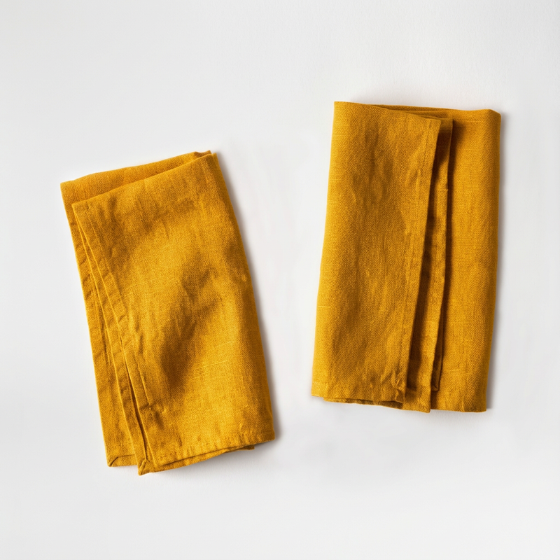 Celina Mancurti Linen Napkins, set of two mustard 100% linen cloth napkins, folded flat lay on white background.