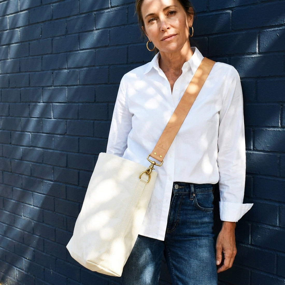 Celina Mancurti Everyday Tote Bag with Tan Leather Strap studio product photo hanging from a wooden wall hook on a neutral…
