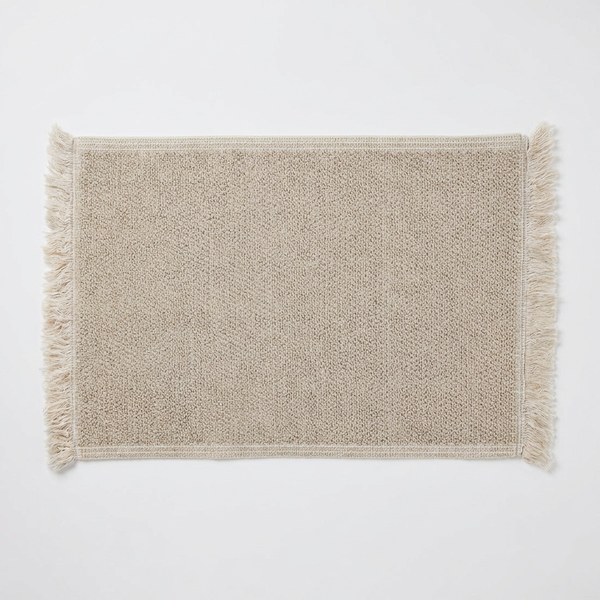 Beige textured bathmat with fringes on a white background