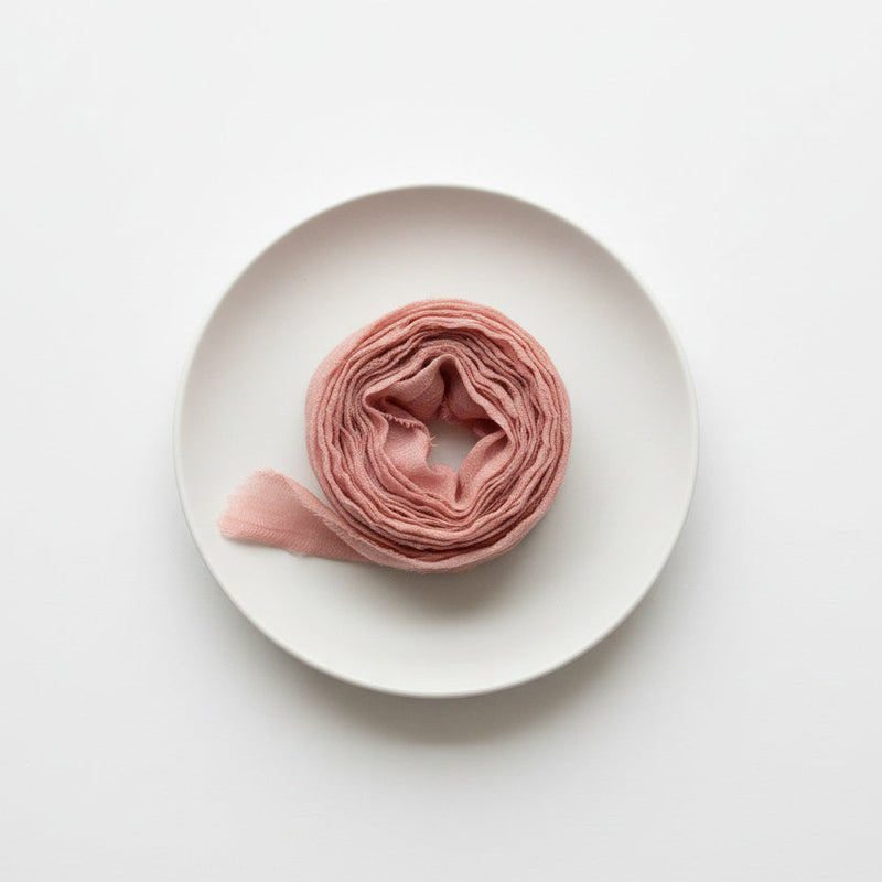 Farmette Plant-Dyed Sari Silk Ribbon, Watermelon pink recycled sari silk, tightly rolled on a white plate, top-down.