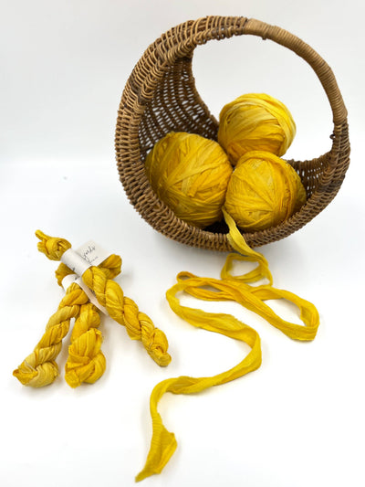 
                    
                      Plant-Dyed Sari Silk Ribbon, Sunflower yellow, recycled silk shown balled in a basket, braided with label, and unwound.
                    
                  