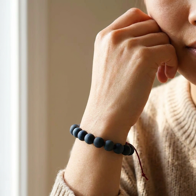 
                    
                      Curious Corners Indigo-Dyed Yakusugi Cedar Beads Bracelet on wrist, showing matte dark blue beads and red Kumihimo cord knot.
                    
                  