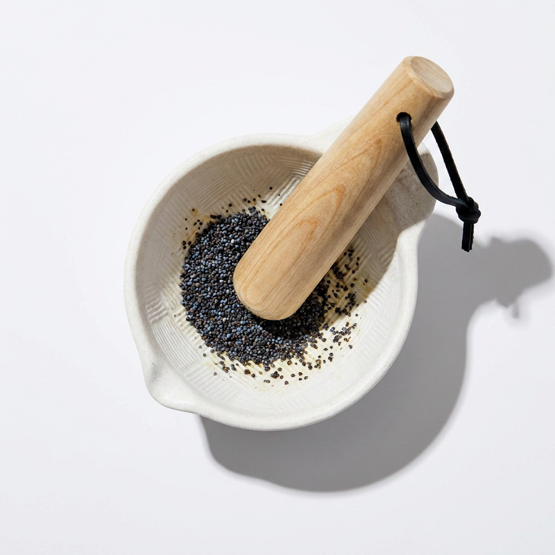 Fort & Field Hinoki Cypress Pestle (Surikogi) with black leather loop, in textured ceramic mortar with poppy seeds, overhead…